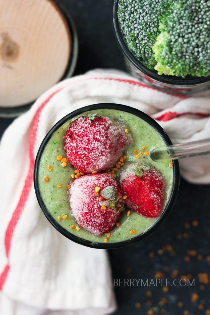 green broccoli smoothie in the glass with strawberries on top