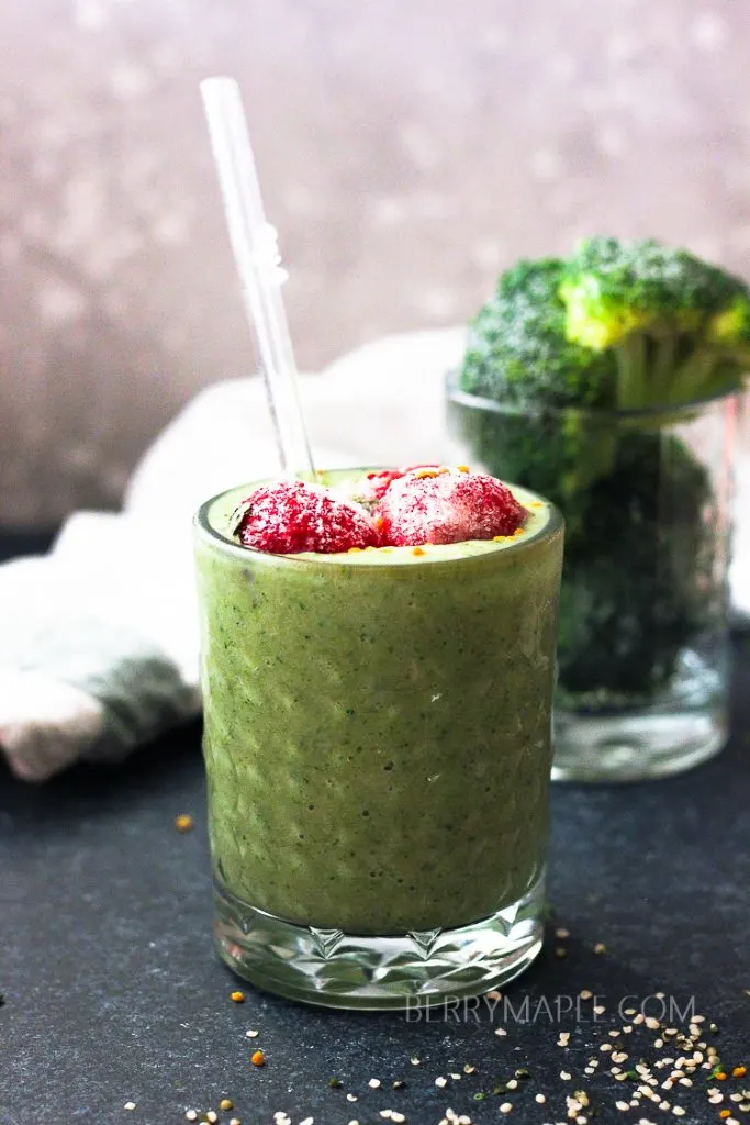 green broccoli smoothie with a srtraw and strawberries on top