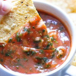 red tomato salsa in a small bowl with a chip dipped