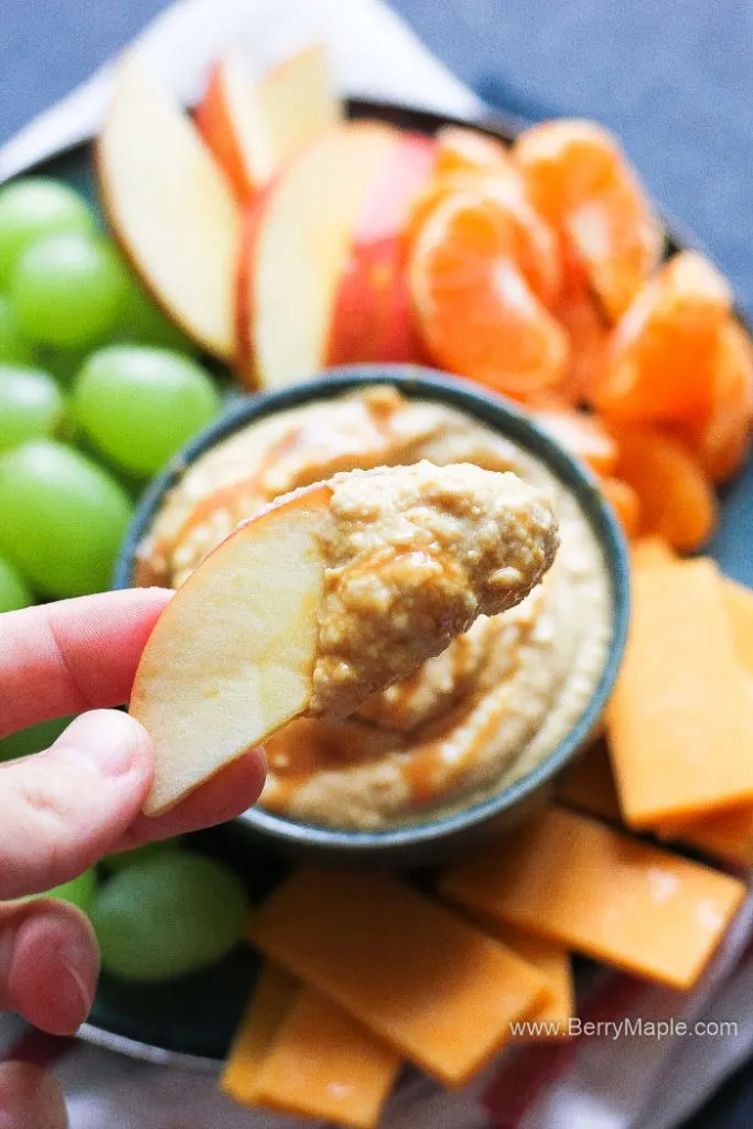 the hand holding a slice of apple dipped in hummus