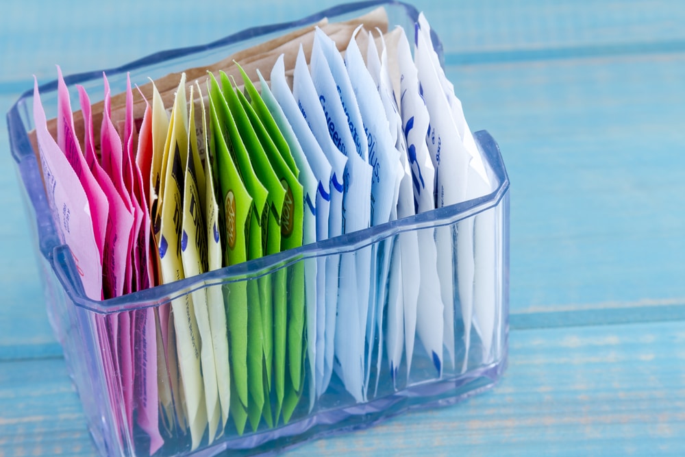 Packets of artificial sweeteners in glass container sitting on bright blue wooden table