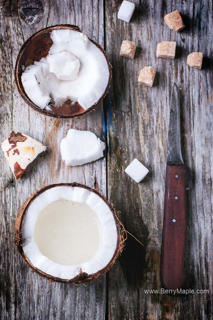 Broken coconut with coconut milk, sugar cubes and vintage knife on old wooden background. Top view