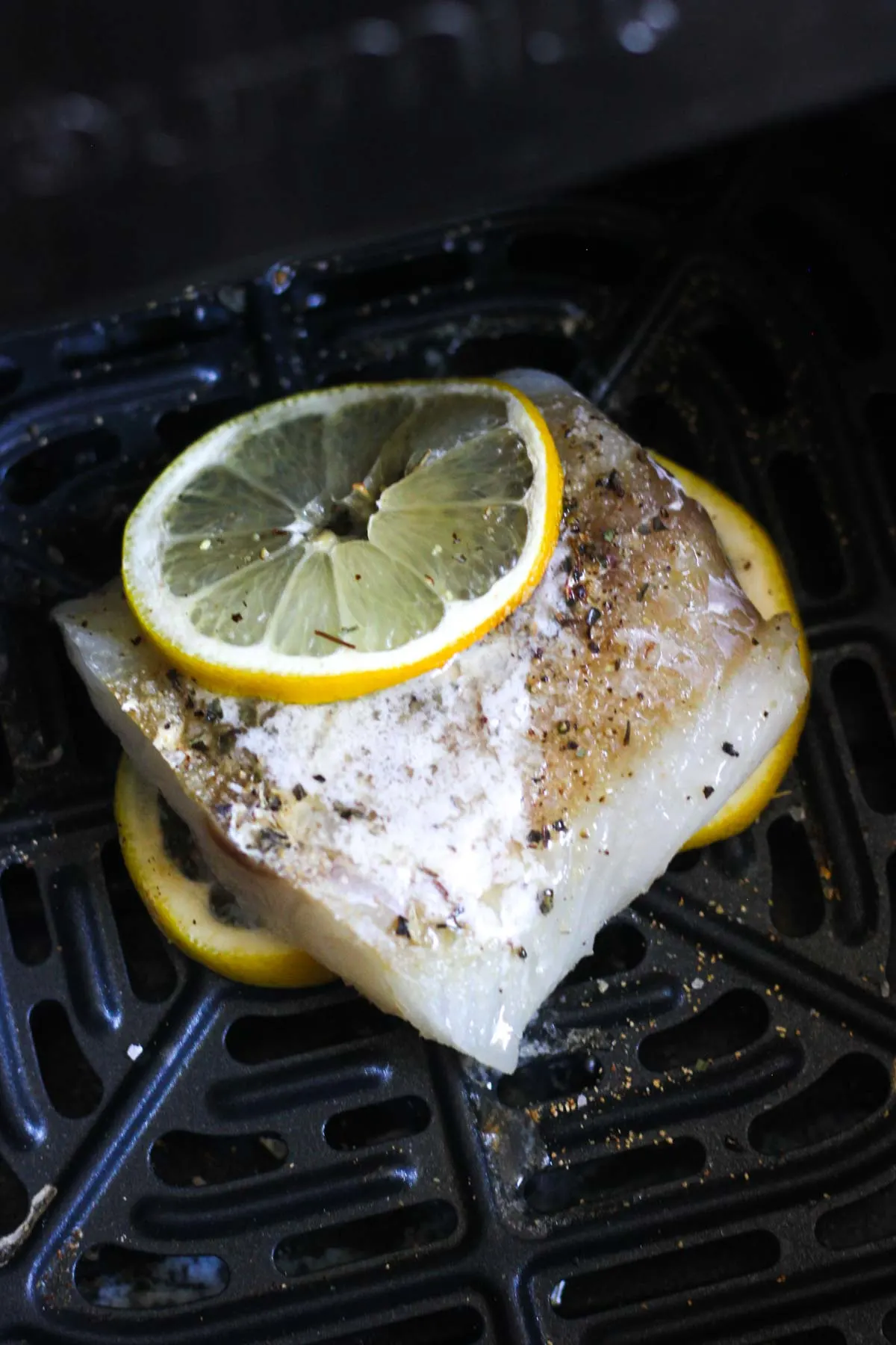 small piece of white cod fish with lemon and black pepper on top