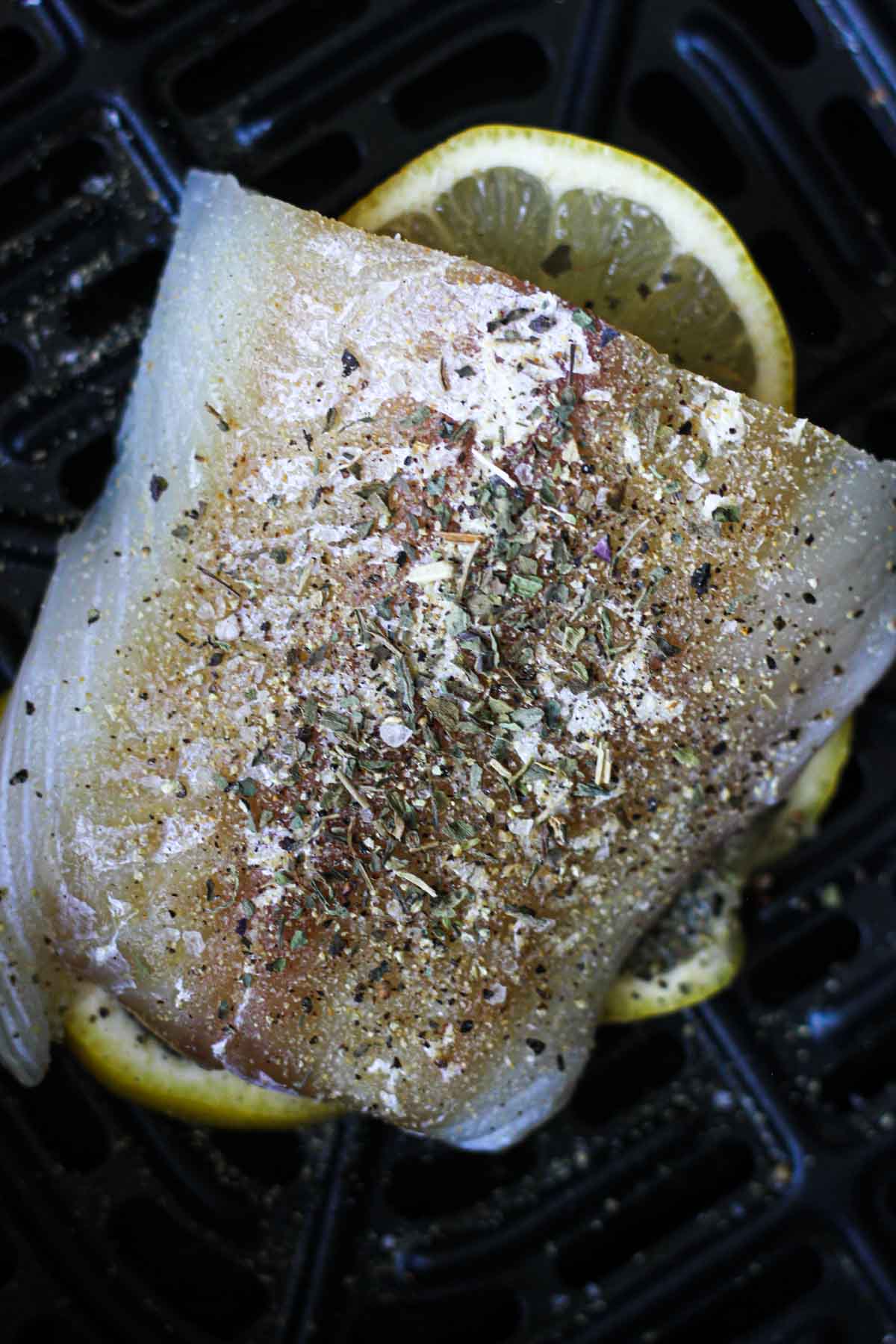 raw cod fillet with spices and lemon in the black air fryer basket