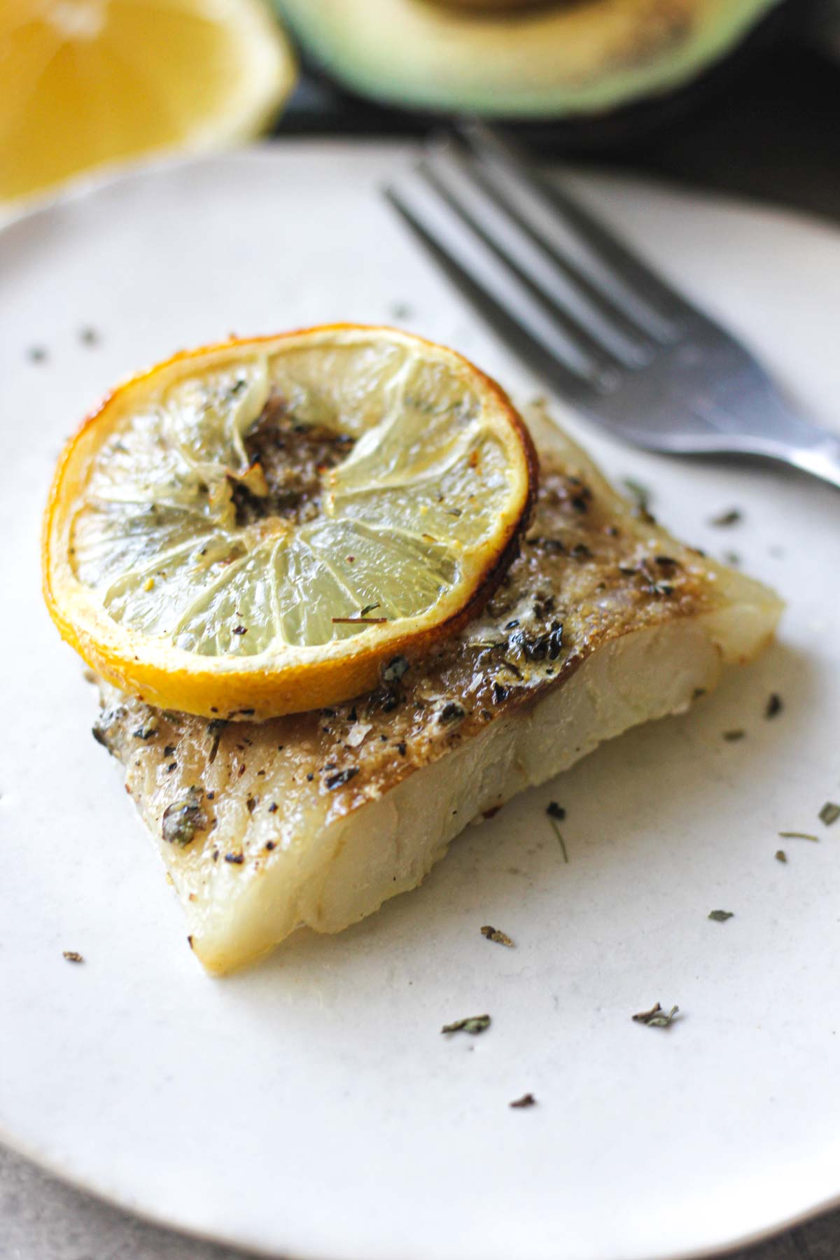 a piece of white fish on a white plate with a lemon slice on top
