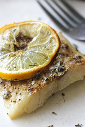 close shot of a cooked cod fillet with a lemon slice on top