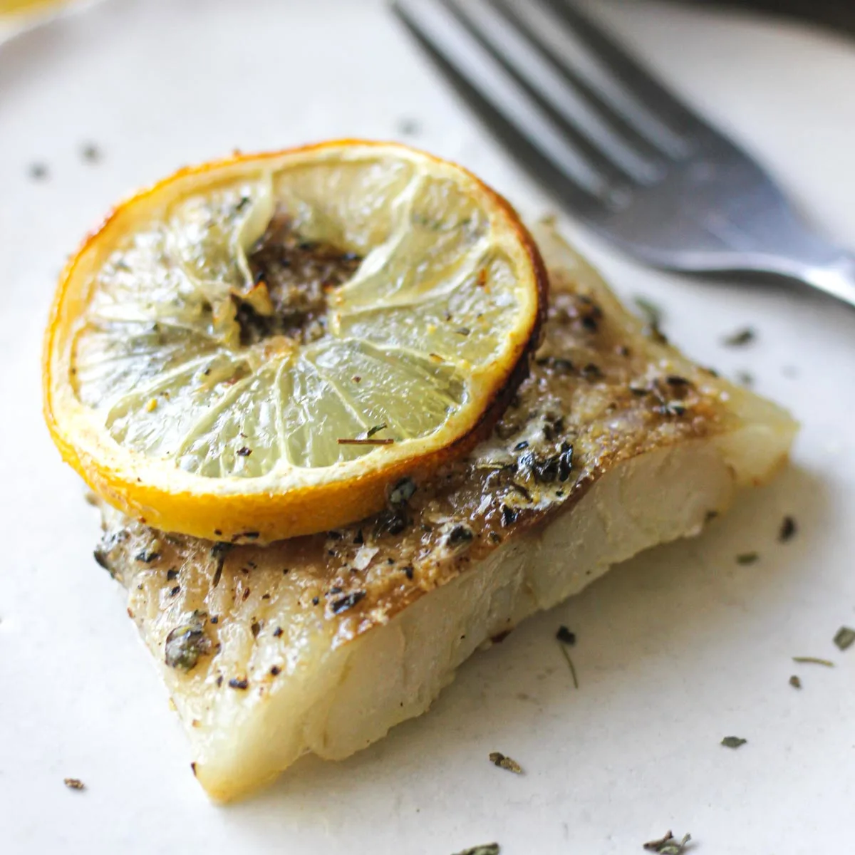close shot of a cooked cod fillet with a lemon slice on top