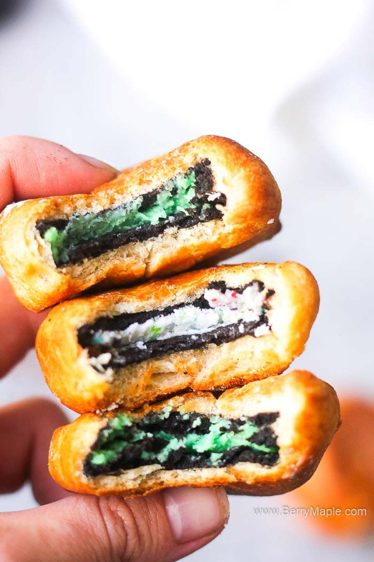 a hand holding a stack of green and funfetti colored oreo cookies wraped in dough
