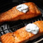 two cooked salmon fillets with white sauce on top in air fryer
