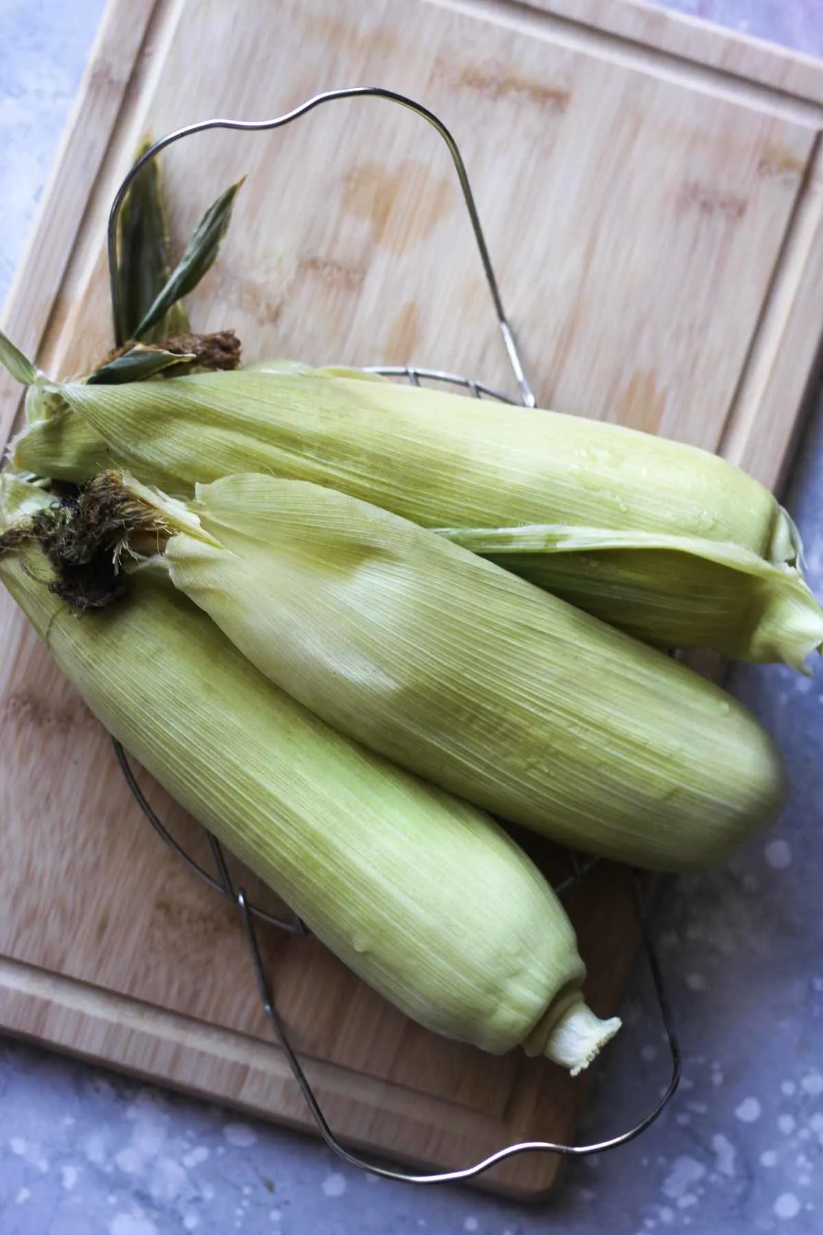 top view of three cooked corn on the cob in husk