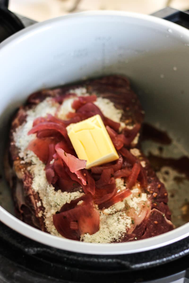 butter on top of meat and red onions in the pot