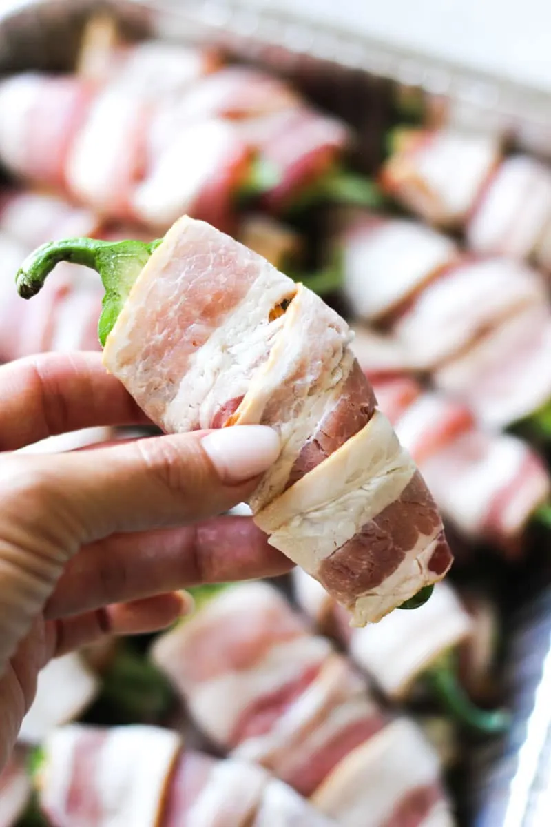 holding a bacon wrapped jalapeno in hand before cooking