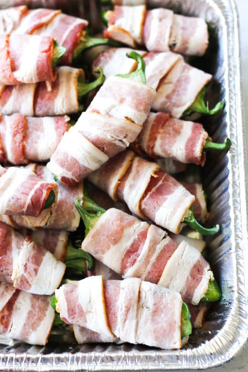 raw wrapped jalapenos in bacon in the tray